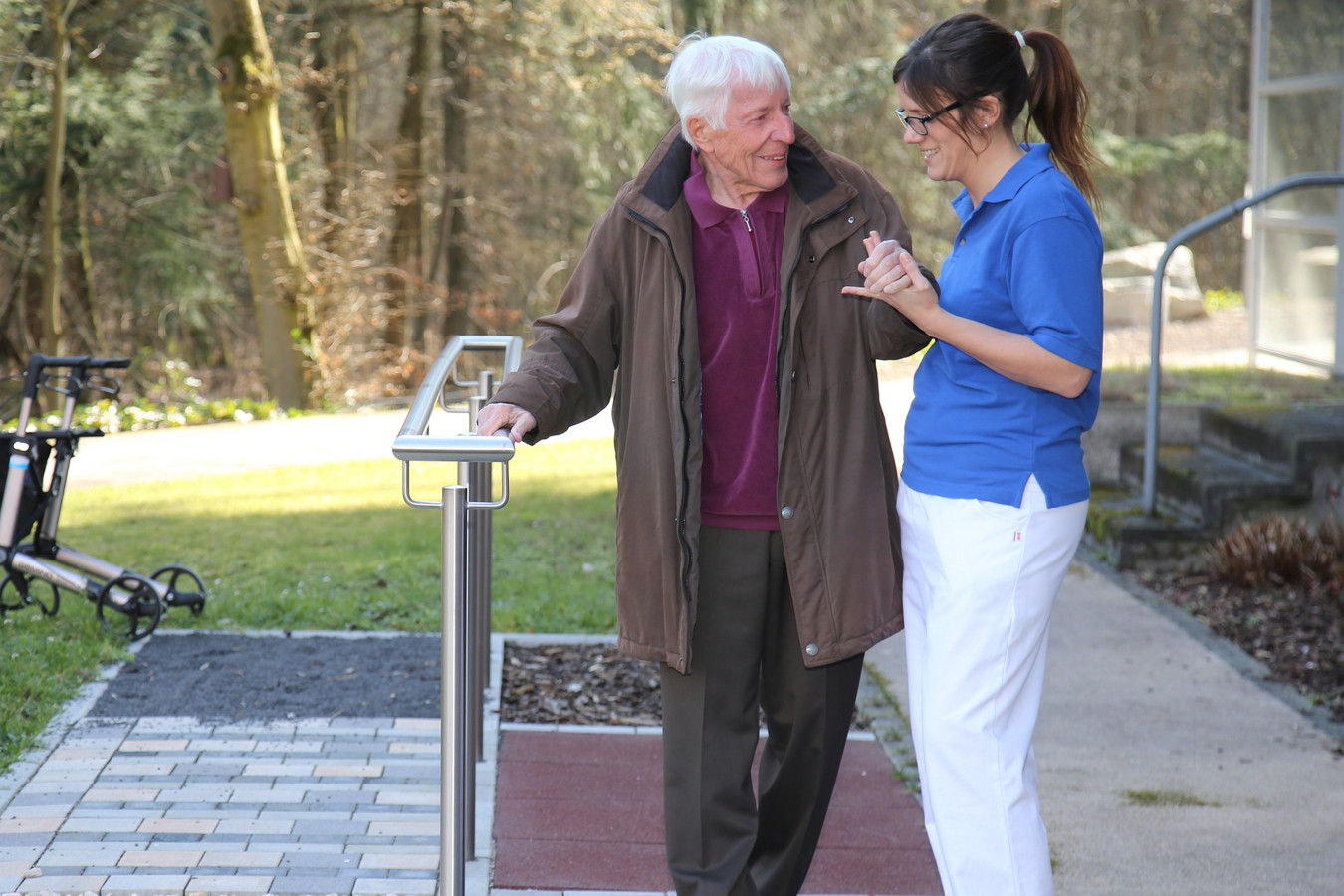 Eine Physiotherpeutin hilft einem älteren Patienten bei Gehübungen. 