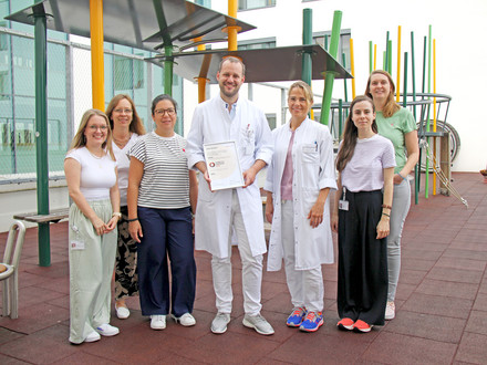 Das Diabetesteam steht auf dem Spielplatz der Kinderklinik und hält das Zertifikat in die Kamera. 